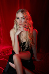 Beautiful blonde woman with long hair on a red velvet background. Hair jewelry on a woman head, modern makeup and arrows on the eyes