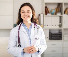 Positive young female trainee doctor undergoing an internship at the clinic stands in a welllit resident's office