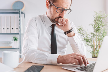 Business person working on laptop computer in bright office interior, serious entrepreneur thinking