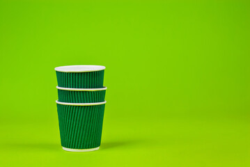 Disposable paper cups on a green background. Ecological coffee utensils. Copy space and free space for text near the glasses.