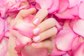 Female hand with glitter pink nail design. Female hand hold spring pink rose petals. Woman hand...
