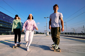 Three excited teenagers spend time in the urban exterior. They are running and skateboarding. - 487297592