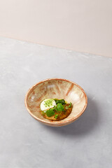 Omelette with creamy espuma, spinach sorbe and green leaves. Omelette in homemade ceramic bowl on gray stone background. Ceramic still life. Breakfast in modern serveware.