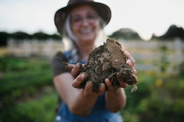 Close up of female famer hands holding soil outdoors at community farm.