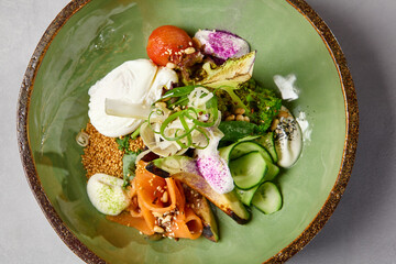 Salad bowl with salmon, avocado, broccoli, vegetables and egg on homemade ceramic plate. Buddha bowl with salmon, broccoli, quinoa in modern serveware. Modern ceramic dishware on concrete background.