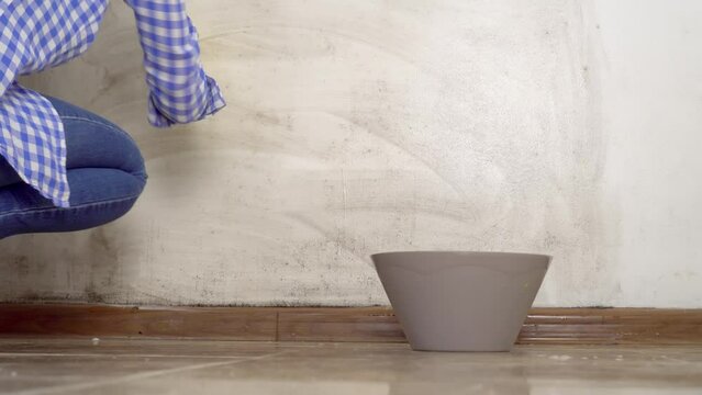 blonde woman washes white walls in an apartment with sponge in yellow gloves. She cleans wall of black mold. damp room. There are cleaning products nearby. concept of cleaning apartment.