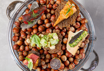 Appetizers set on luxury plate with hazelnut. Creative platter of appetizers from inspirational chef. Salmon cheesecake, fish tartar, pastrami crocket, liver pate, baked mini-paprika
