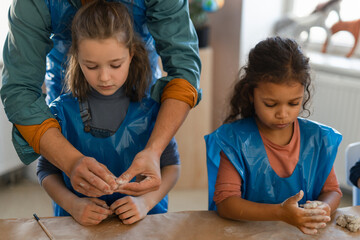 Little kids with teacher working with pottery clay during creative art and craft class at school.
