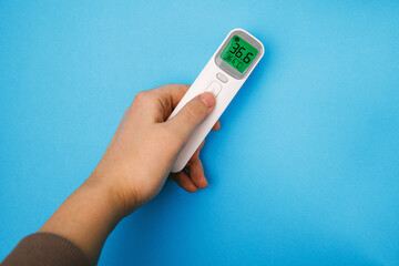 Non-contact infrared thermometer isolated on blue background. Hand holding thermometer. Anti virus...