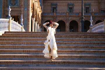 Flamenco dancer, woman, brunette and beautiful typical spanish dancer is dancing and clapping her hands on the stairs of a square in seville. Flamenco concept of cultural heritage of humanity. - obrazy, fototapety, plakaty