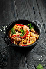 Japanese stir fryed udon noodles in wok. Udon noodle with chiken and vegetables on wooden background. Asian noodles on black table with ingredients. Wok menu.