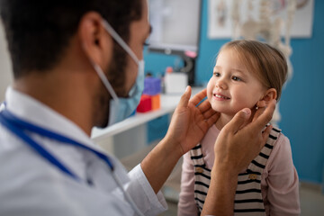 Young male doctor checking little girl's lymph nodes in his office.