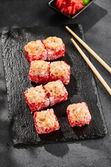 Baked Maki sushi on dark slate. Hot sushi roll with salmon. Sushi roll with tobiko outside, baked fish  and cheese topped. Style concept japanese menu with black background, leaves and hard shadow.