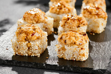 Baked Maki sushi on dark slate. Hot unagi maki with eel. Sushi roll with baked eel, cheese and unagi sauce topped. Style concept japanese menu with black background, leaves and hard shadow.