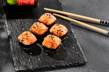 Baked Maki sushi on dark slate. Hot unagi maki with tobiko. Sushi roll with baked cheese, masago and unagi sauce topped. Style concept japanese menu with black background, leaves and hard shadow.