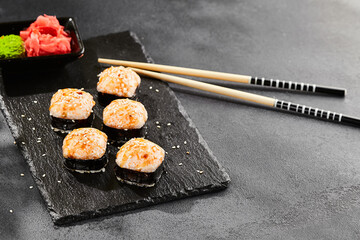 Baked Maki sushi on dark slate. Hot unagi maki with tobiko. Sushi roll with baked cheese, masago and unagi sauce topped. Style concept japanese menu with black background, leaves and hard shadow.
