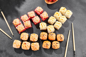 Hot maki set on dark slate. Baked sushi set with variety rolls. Sushi rolls with salmon,tobiko, crab and baked cheese topped. Style concept sushi menu with black background, leaves and hard shadow.