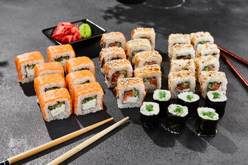 Maki sushi set on dark background. Maki set with variety rolls. Composition from popular sushi rolls and hosomaki. Style concept sushi menu with black background, leaves and hard shadow.