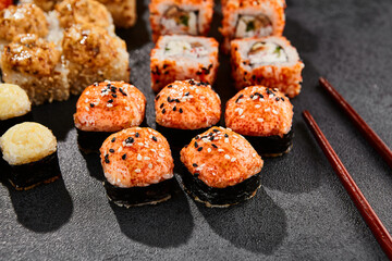 Maki sushi set on dark background. Maki set with variety rolls. Composition from sushi rolls and baked maki . Style concept sushi menu with black background, leaves and hard shadow.