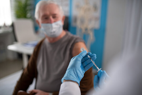 Close-up of doctor holding covid-19 vaccince syringe and preparing to give it to senior man.