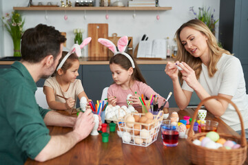 Happy caucasian family of four people decorates easter eggs at home