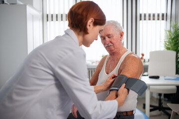 Fototapeta premium Female doctor measuring blood pressure to senior man patient in her office.