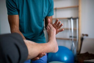 Close-up of physiotherapist exercising with senior patient's leg in a physic room.