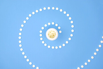 Pills spiral and drug bottle on blue background. Spiral made of round white tablets and plastic...