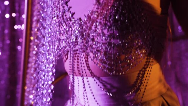Young slim woman in beautiful evening dress in neon purple light in the evening. Sparkling silver evening dress with rhinestones and beads.