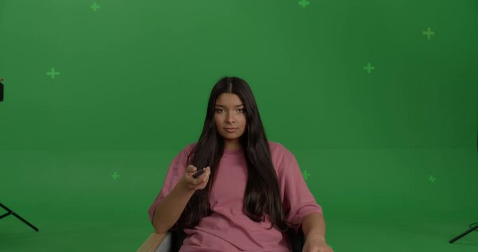 GREEN SCREEN CHROMA KEY Young female sits in front of TV screen in an armchair with a remote, gets blown away
