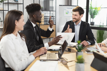Positive business colleagues gesturing thumbs up during conference meeting at modern office. Deal, approve and successful cooperation concept.