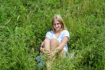 blonde girl sits in the grass in a field in nature in summer