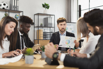 Multi ethnic team of competent financiers wearing stylish formal clothes gathering at boardroom for urgent brainstorming. Concept of business, people and cooperation.