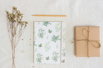 Notebook with flowers, pencil and a brown box over the white fabric.