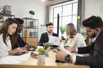 Multi ethnic team of competent financiers wearing stylish formal clothes gathering at boardroom for urgent brainstorming. Concept of business, people and cooperation.