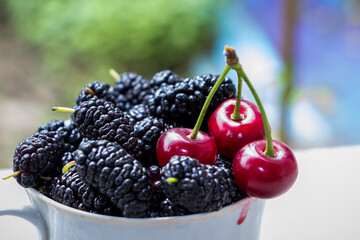 black mulberry and red cherries in a cup outdoors in the garden