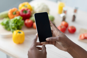 Hands of young african american woman hold smartphone with blank screen making photo on table
