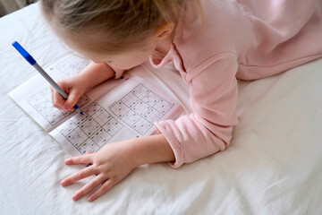 A little girl (preschooler) solves a children's crossword. Tasks and puzzles for the development of...