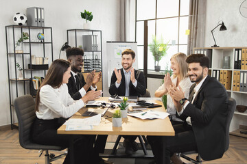 Successful business colleagues applauding during conference meeting at modern boardroom. Multiracial partners feelings happiness while reaching common consensus.