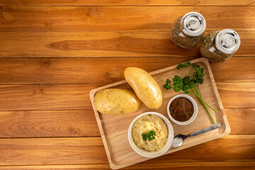 Top view photo of mashed potatoes dish menu with brown gravy serve in wooden tray with some parsley, and seasoning on wooden table background backdrop. Eatable recipe healthy appetizer concept ideas