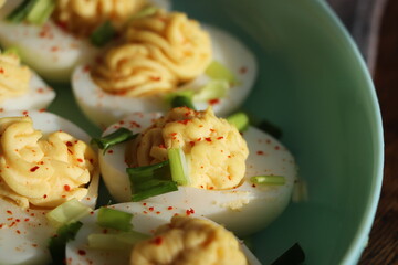 Deviled Eggs sprinkled with paprika and chopped green onion on a green plate on a woodene table . Top view