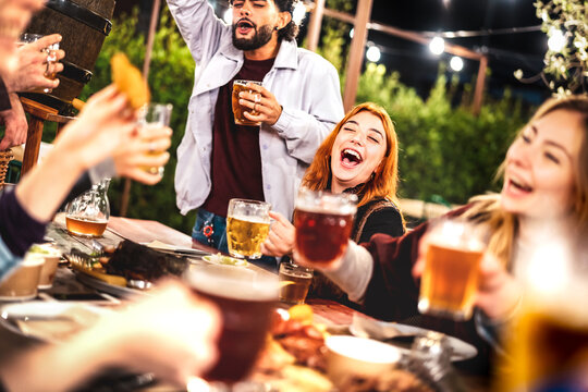 Young men and women having fun drinking out at beer garden patio - Social gathering life style concept on happy people enjoying hangout time together at night - Warm filter with shallow depth of field