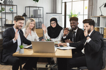 Group of multiracial company workers smiling and waving during conference call on modern laptop. Five business colleagues having online meeting at boardroom.