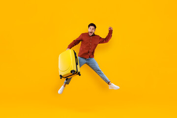 Male Traveler Jumping Holding Big Suitcase Over Yellow Background