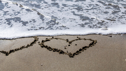 Foamy sea wave erasing two heart drawings on beach sand
