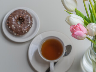 donuts, a cup of coffee, and tulips on top. Concept, breakfast and spring, holidays, spring holiday.