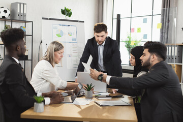 Group of busy multiracial people in formal clothes having active discuss during meeting at office. Men and women sitting at desk, using modern gadgets and examining various documents.