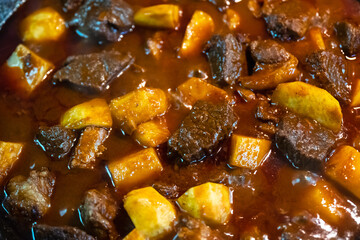 Cooking goulash with beef, potatoes, tomato and paprika in deep frying pan at home kitchen. Food...