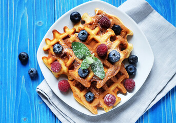 Homemade Belgian waffles served with fresh berries on white plate over wooden background, close up.
