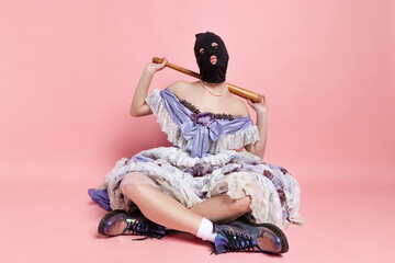 Comic portrait of young funny girl in image of medieval royal person in renaissance style dress and black balaclava isolated on pink background. Comparison of eras, beauty